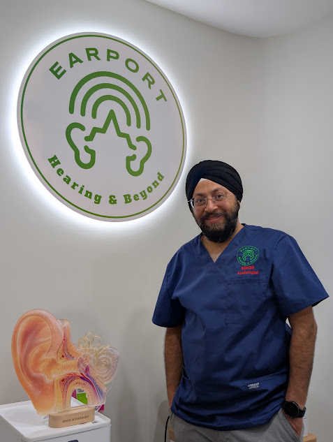 Earport Audiology clinician standing beside an ear anatomy model and Earport Hearing & Beyond clinic sign