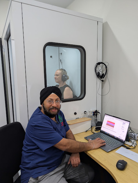 Earport Audiology clinician conducting a controlled hearing assessment while a patient sits inside a sound-treated testing booth